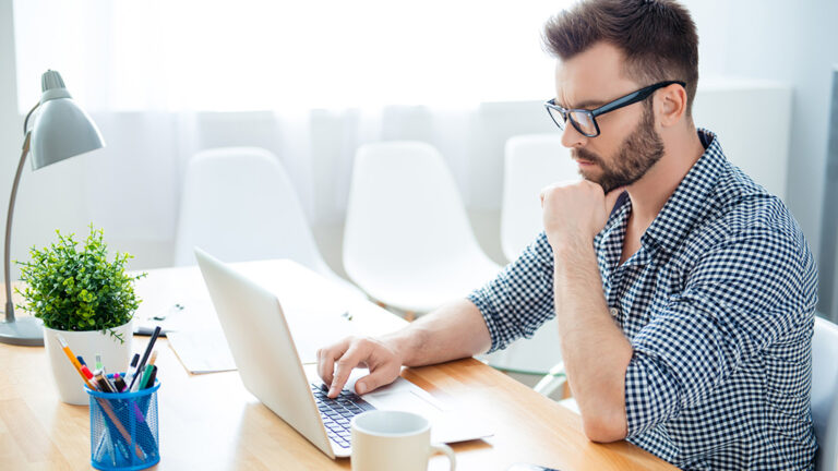 A bearded, middle-aged man with light skin tone sits looking intently at laptop.